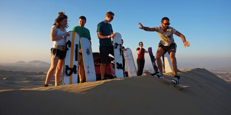 grupo de amigos fazendo sandboarding no deserto de huacachina - roteito peru 8 dias