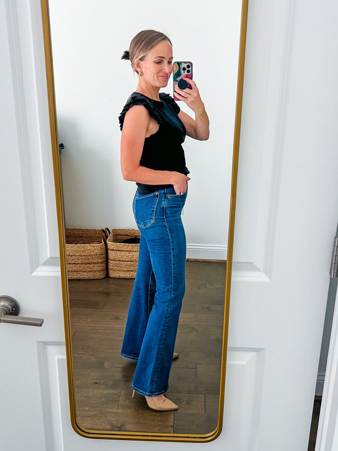 Woman showing the side details of jeans in Ultra High Rise Flare Jean in black and dark blue wash