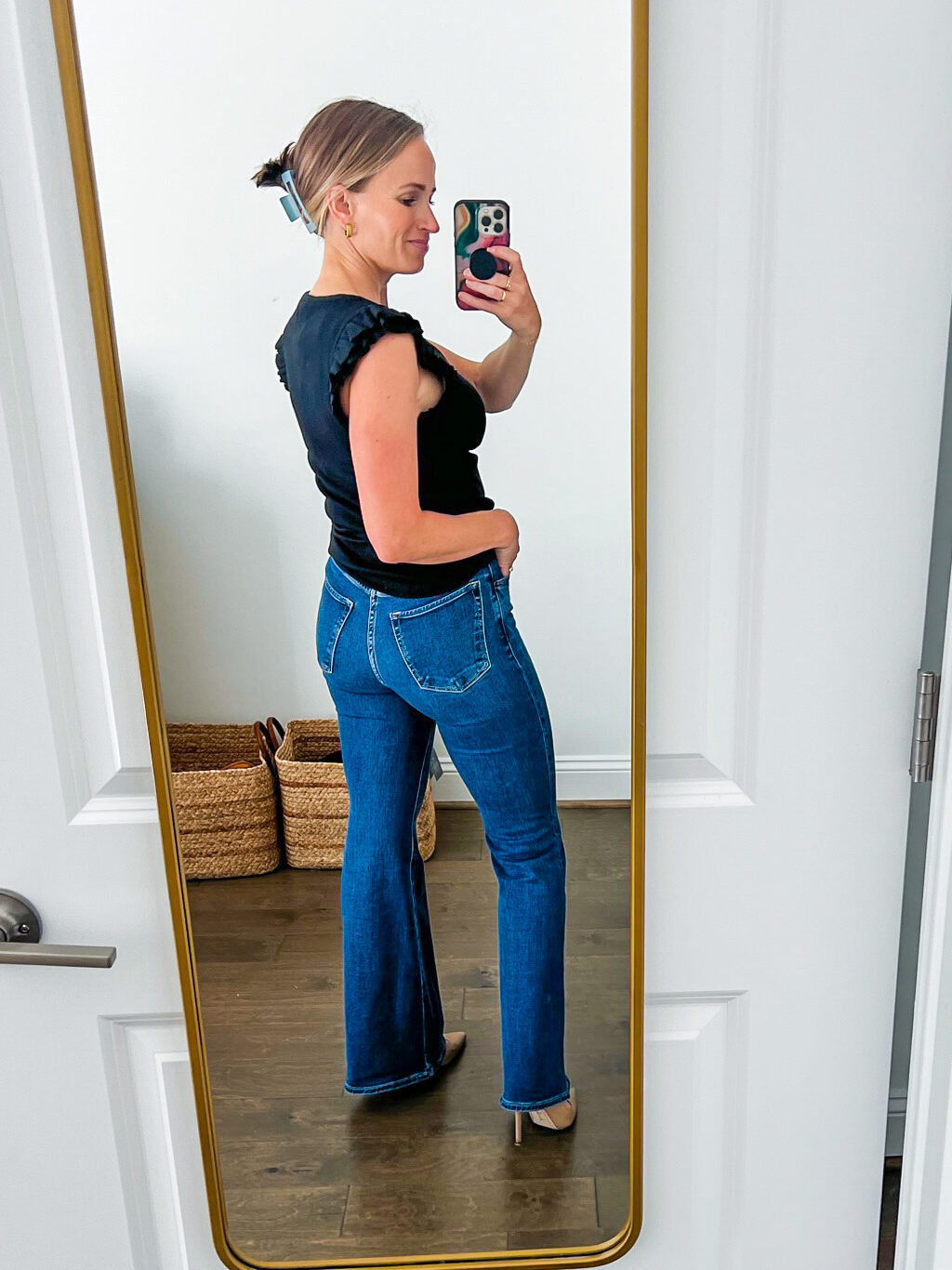 Woman showing the back details of the Ultra High Rise Flare Jean in black and dark blue wash