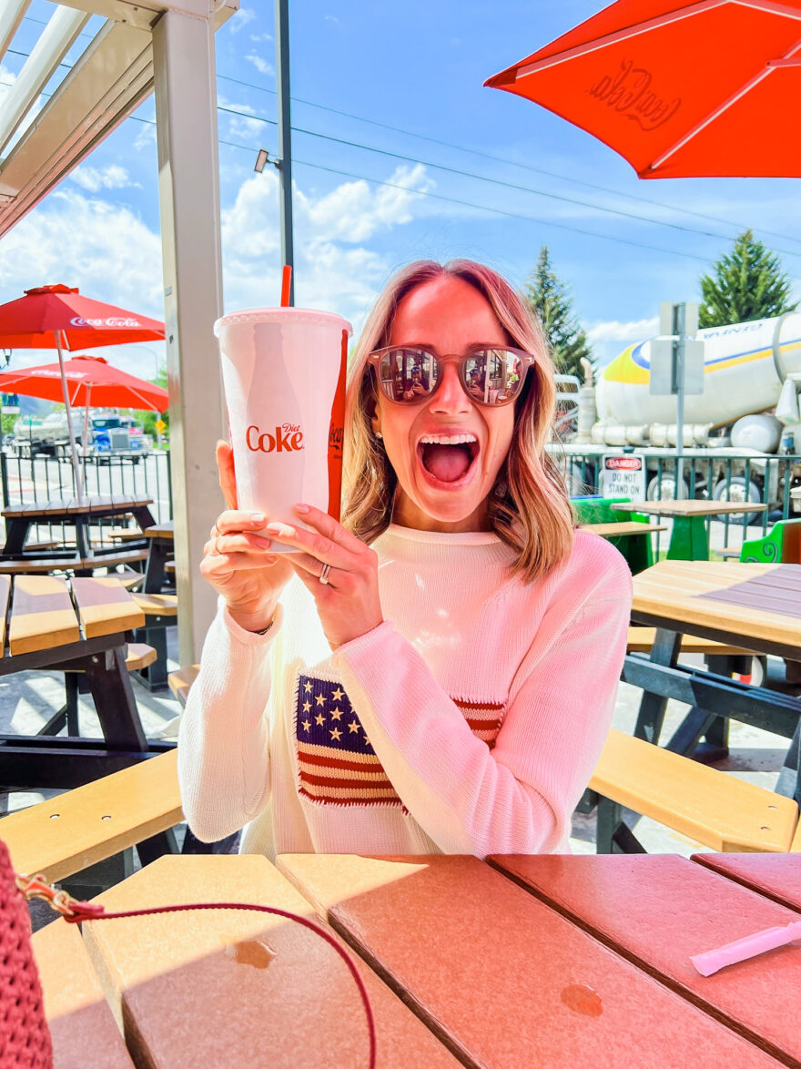 woman holding a glass of coke and wearing Tuckernuck blouses from Ivory Americana Sweater