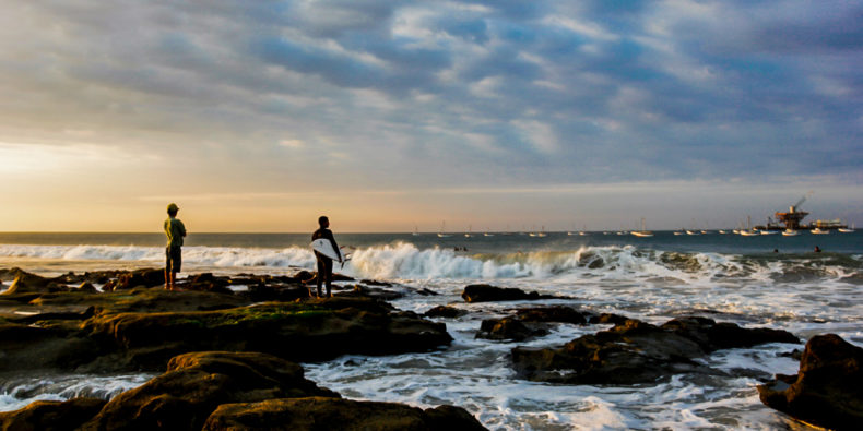 Un surfeur debout sur la plage face à la vague de Cabo Blanco dans le nord du Pérou.