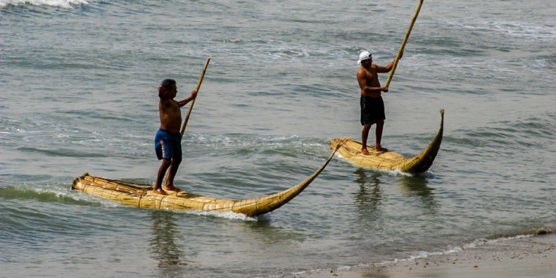 Des pêcheurs debouts sur leur canoë en roseau de totora à Huanchaco dans le nord du Pérou.